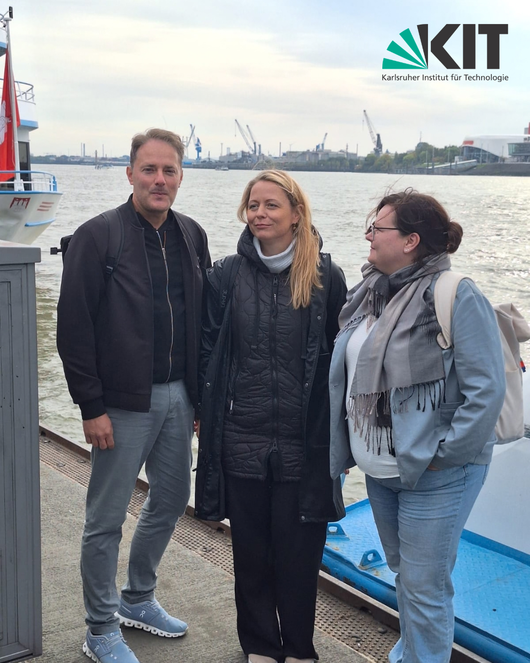 "Drei Personen vor KIT-Logo am Hafen mit Schiff im Hintergrund."