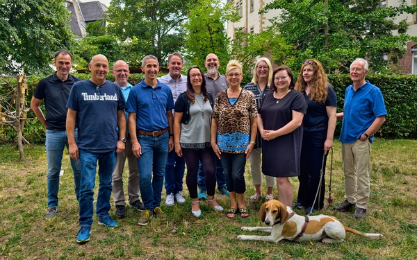 Gruppe von Menschen im Freien, Hund liegt vorne auf dem Boden.