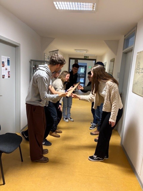 Gruppe junger Menschen in einer Flurhalle, zwei Parteien reichen sich die Hände in einem freundlichen Austausch.